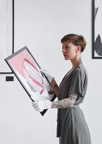 A woman holding and admiring a piece of artwork in a gallery.