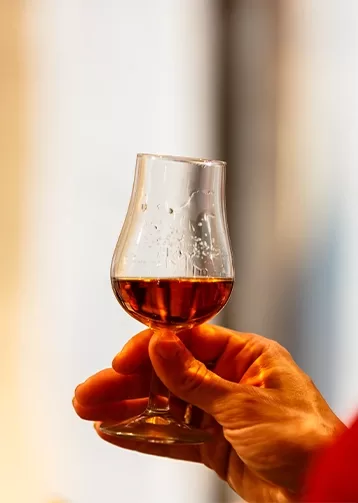 A hand holding out a glass filled with alcohol.