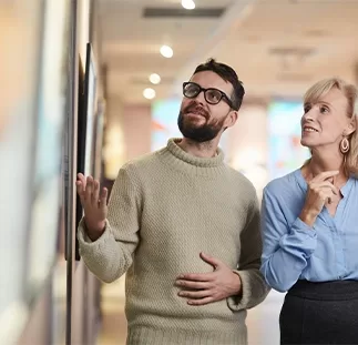 A man showing a woman a piece of art on the wall in an art gallery.