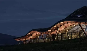 A beautiful building with a waved roof lit up.