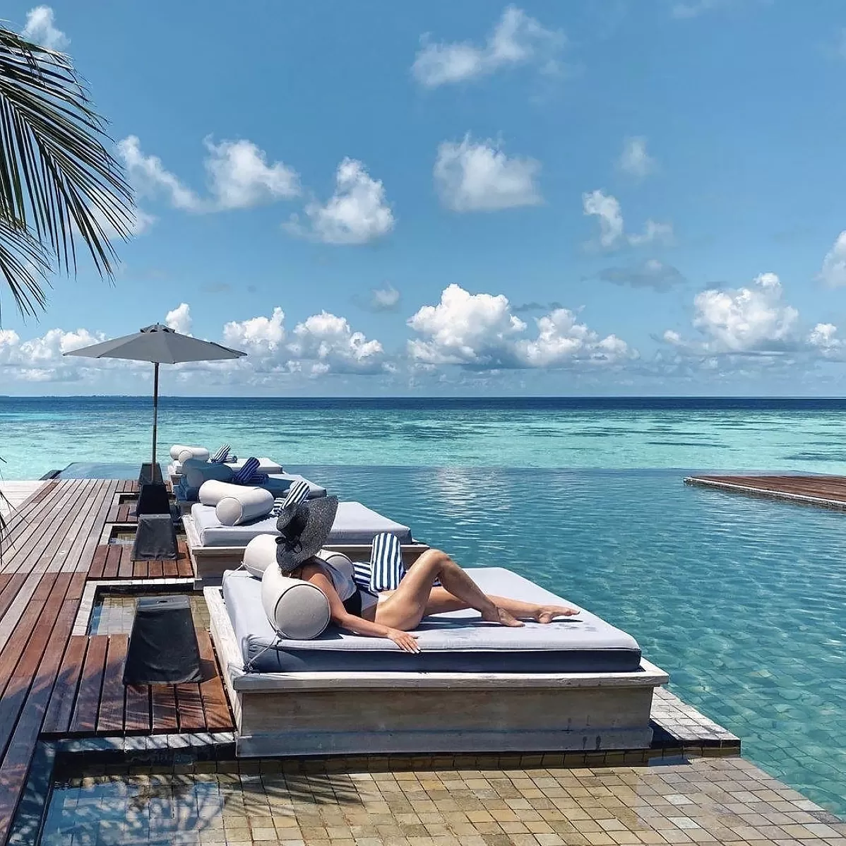 Women sunbathing with panama hat on luxury sun bed-lounger on patio facing blue sea oasis at Raffles, Maldives