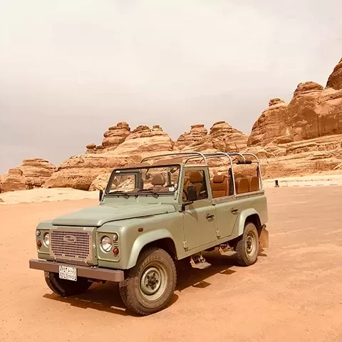 Sage green 4x4 car on the sand in front od desert rocks in Alula, Saudi Arabia