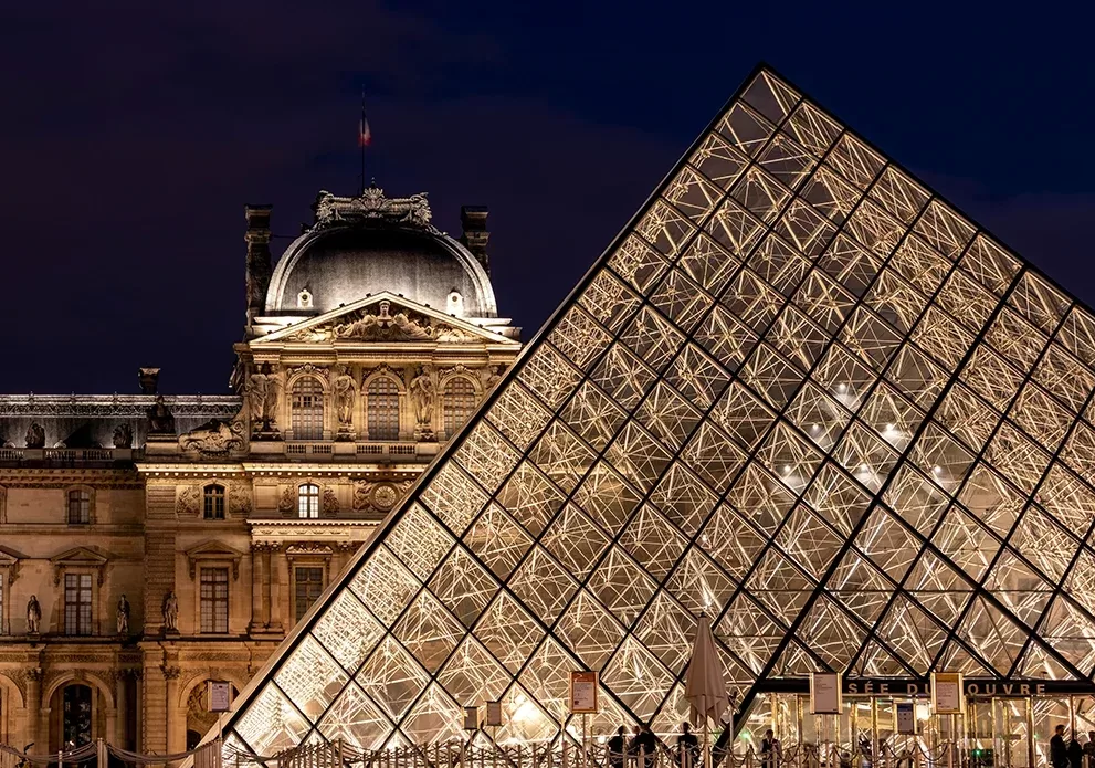Lit-up view of The Louvre and historic buildings at night, Paris.