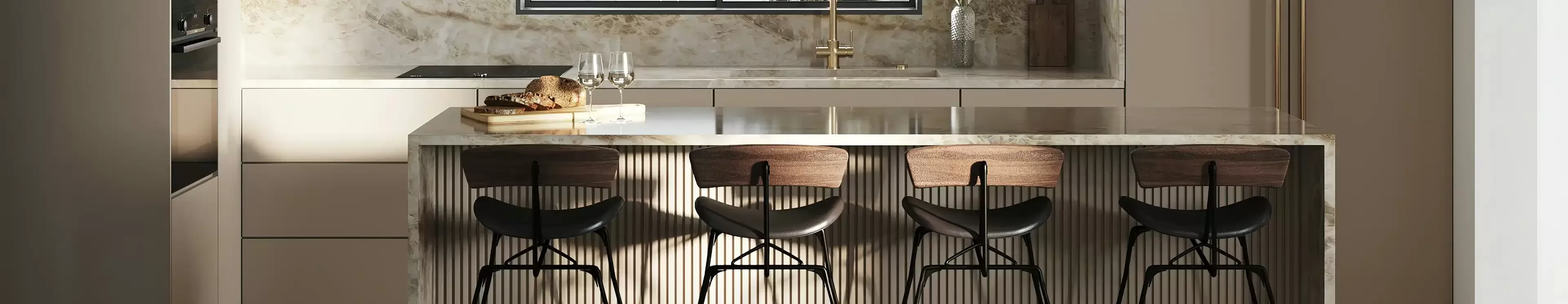 Modern kitchen with sleek beige cabinetry and marble backsplash. A large island with a ribbed front features three stylish bar stools and a countertop adorned with bread and wine glasses. Three spherical pendant lights hang above the island, and a window offers natural light.