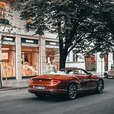 Red convertible Bentley driving through retail street