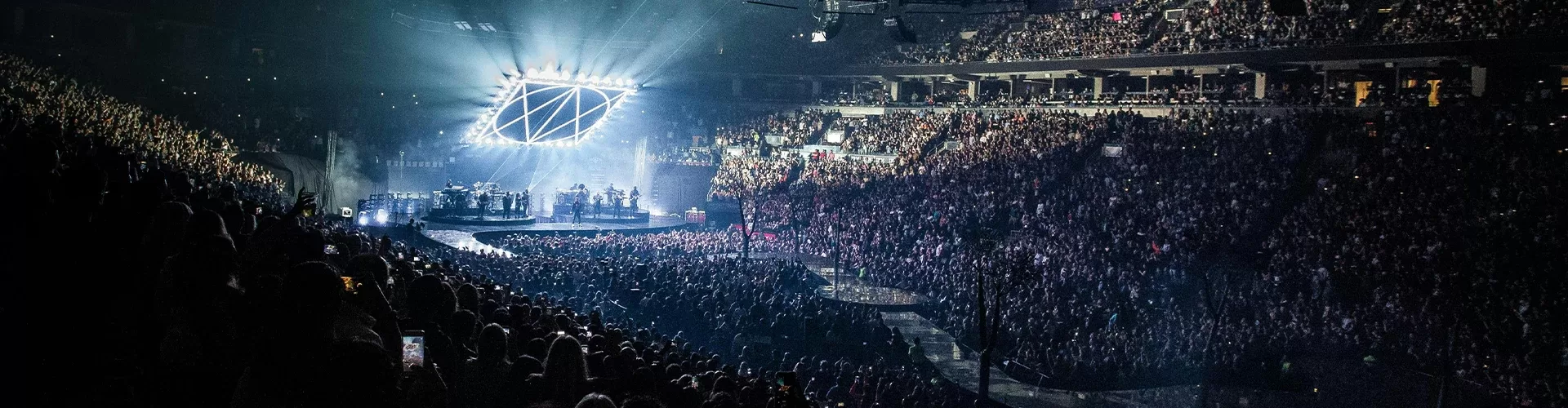 A vibrant concert atmosphere featuring a massive cheering audience, bright stage lights, and musicians playing passionately.