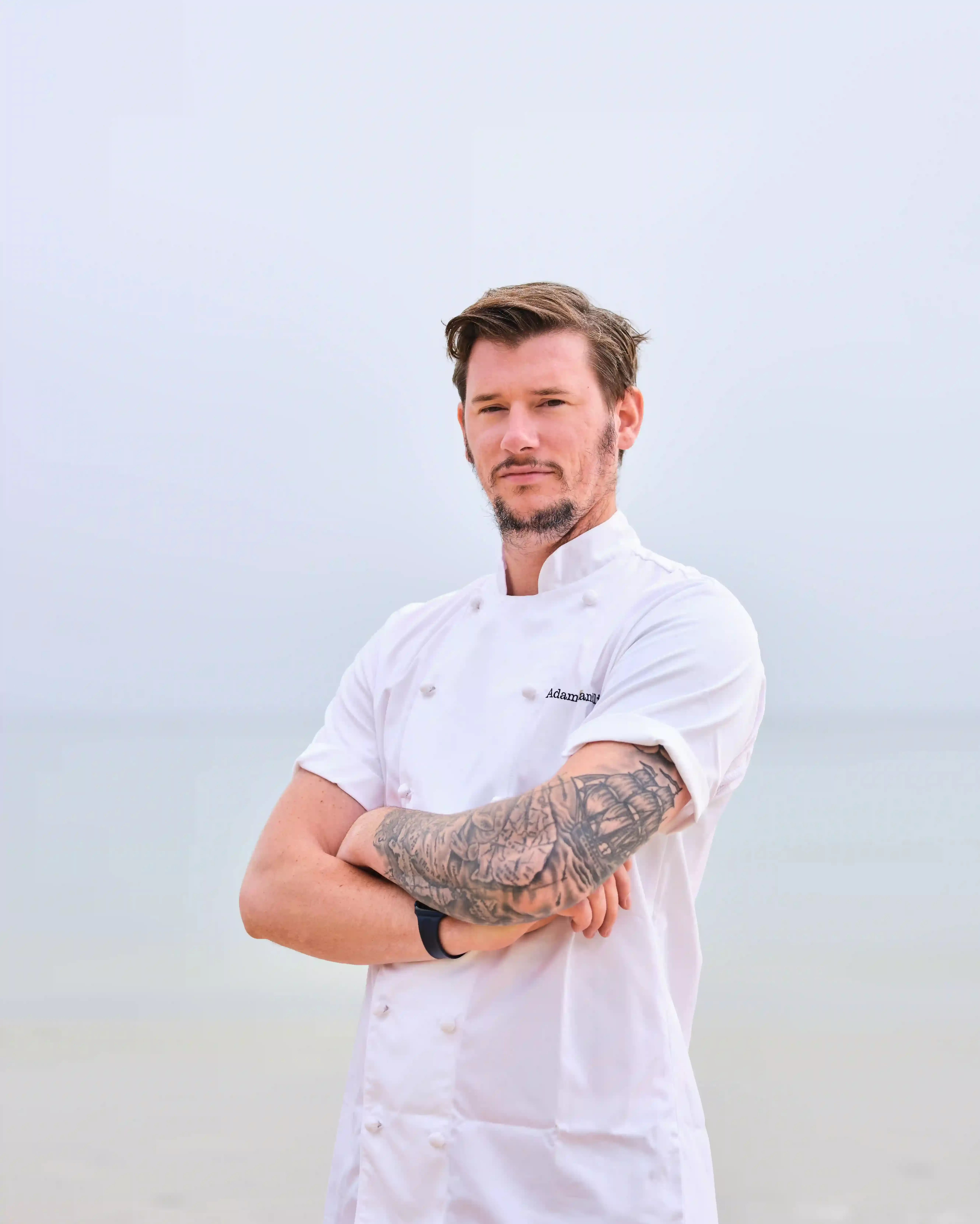 Photo of Adam Handling, Michelin star chef in his white chef uniform crossing his arms.