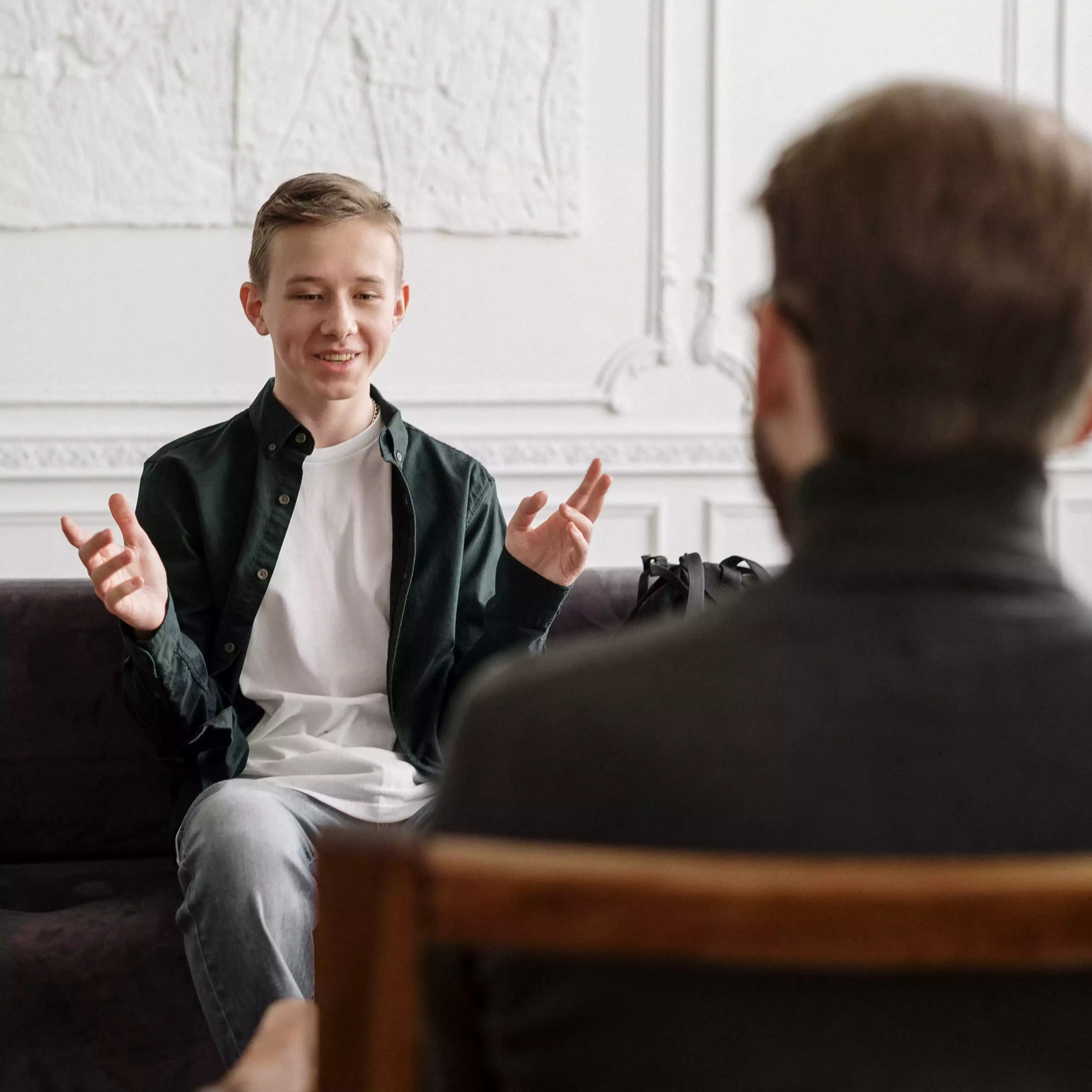 Boy sat on chair opposite adult on chair smiling making hand gestures