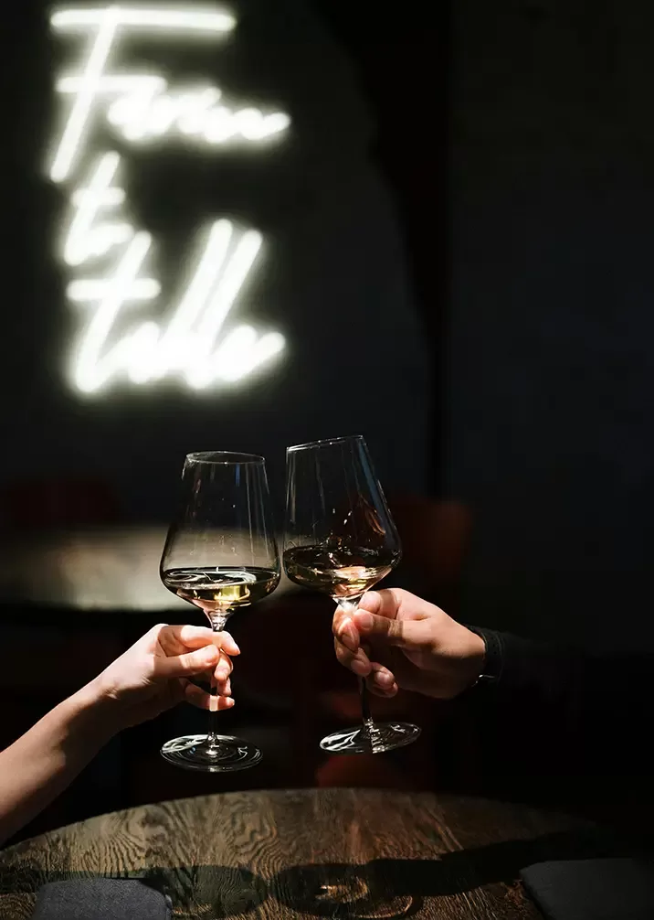 A glass of red wine with a rich colour, reflecting light, set against a blurred background of a vineyard.