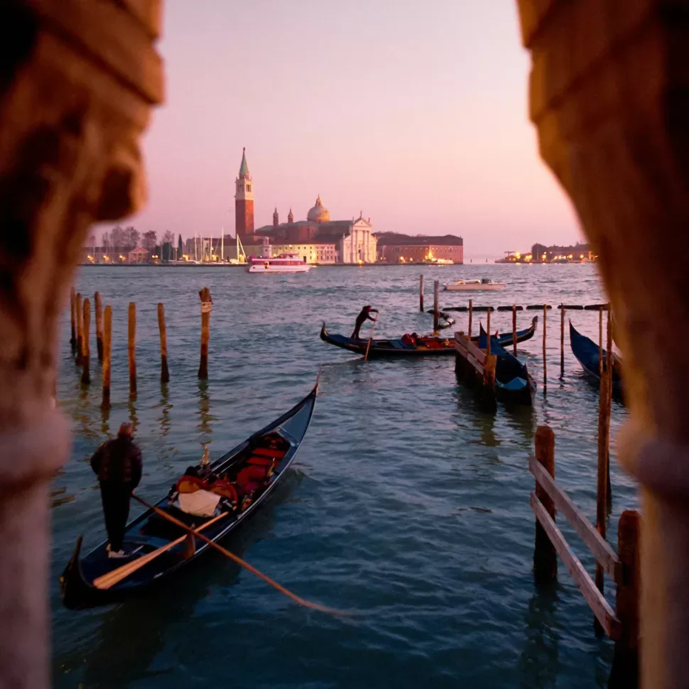 Gondolas floating on the water at sunset in Venice, with buildings and a bell tower in the background.