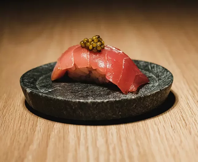 A marble plate with one piece of fresh salmon sushi on it.