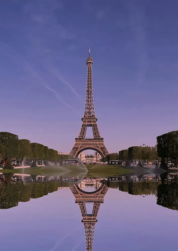 The Eiffel Tower stands tall in the distance, beautifully reflected in a serene pond below.