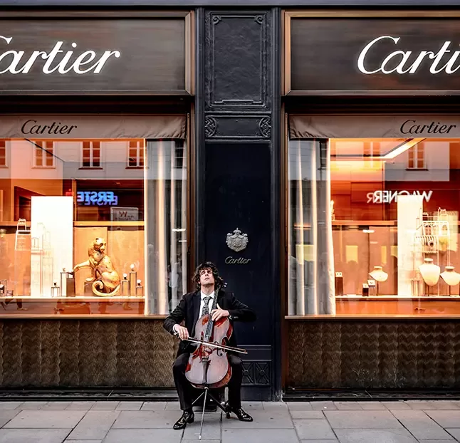 A musician performs on the cello in front of a Cartier boutique, blending art and luxury in an outdoor setting.