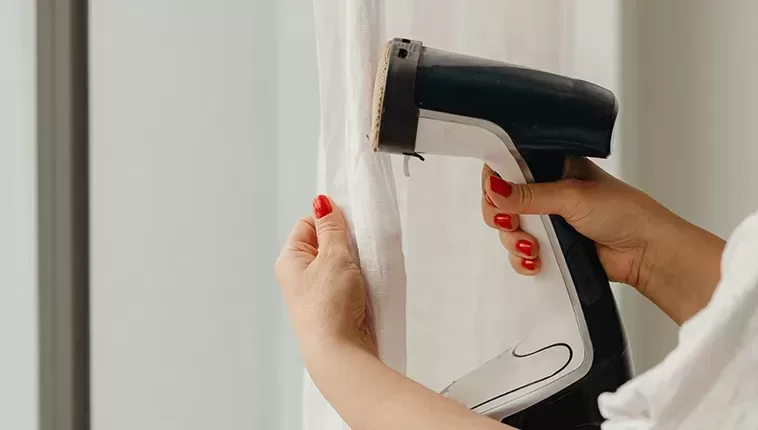 A person carefully ironing a curtain with a steam iron, ensuring smooth and wrinkle-free fabric.