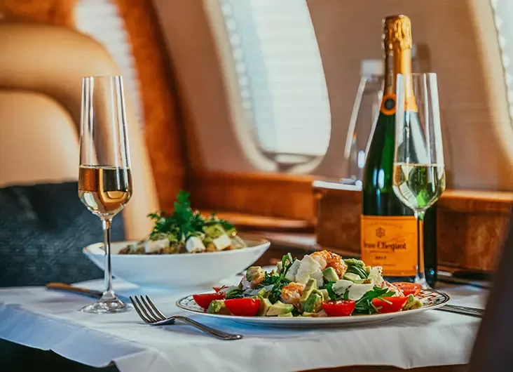 A gourmet meal served on an airplane tray, accompanied by a glass of wine and a flute of champagne.