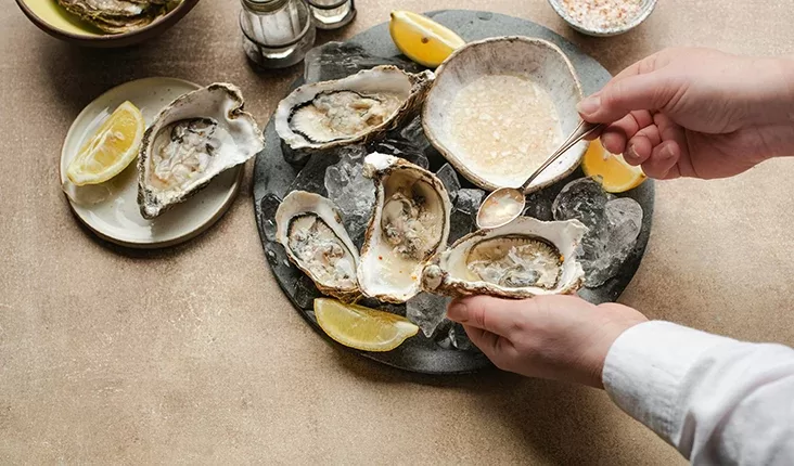 Person eatting from a bowl filled with oysters and lemon wedges.