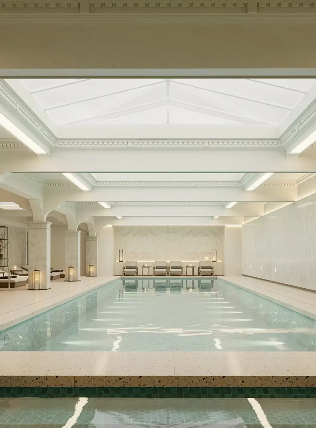 A serene indoor swimming pool in a spacious, elegant room with a high glass ceiling, soft lighting, light-colored walls, and several lounge chairs at the far end.