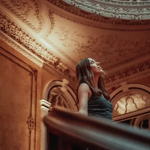 A woman looking up in an ornate, decorative interior with detailed architectural elements and soft lighting.