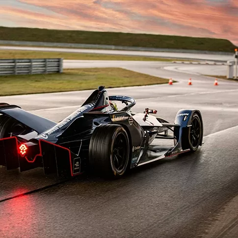 Electric race car on a wet track during sunset, showcasing innovation and speed.