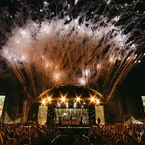 A vibrant stage illuminated by colorful fireworks, creating a festive atmosphere for the audience.