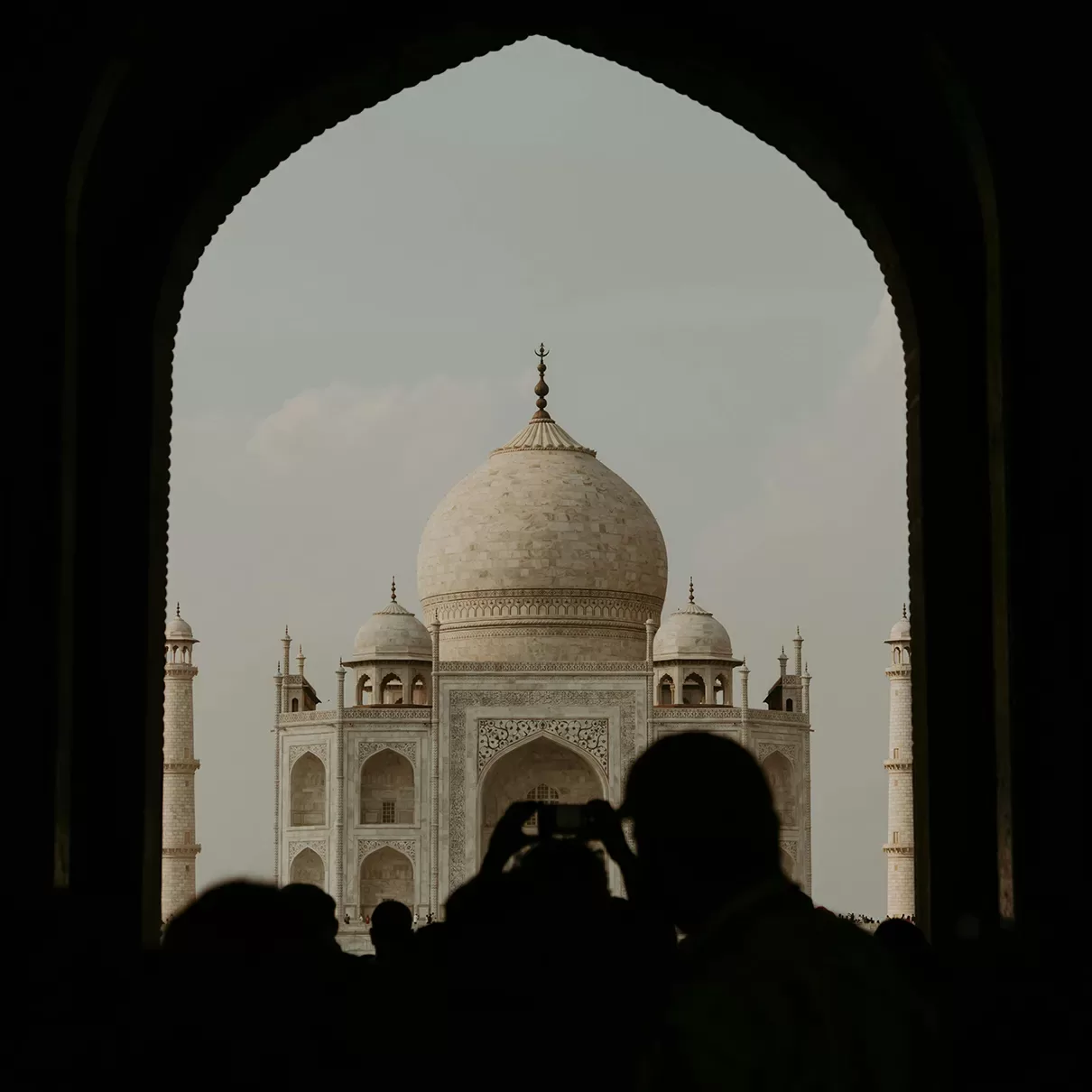 A majestic view of the Taj Mahal framed through an arched entrance, with a crowd silhouetted in the foreground.