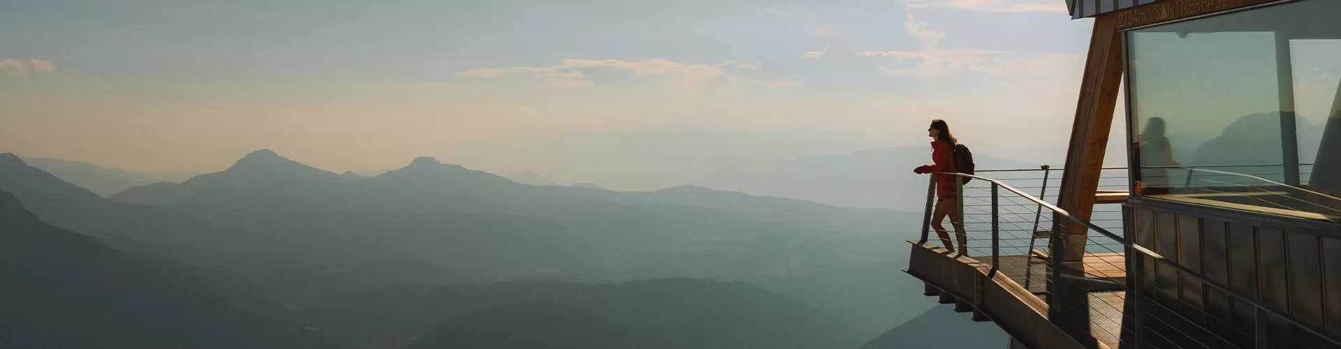 A man stands on a balcony, gazing at the majestic mountains in the distance, surrounded by a serene landscape.