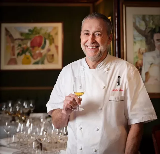 A professional chef in a white uniform skilfully preparing a gourmet dish in a modern kitchen setting holding a champagne.