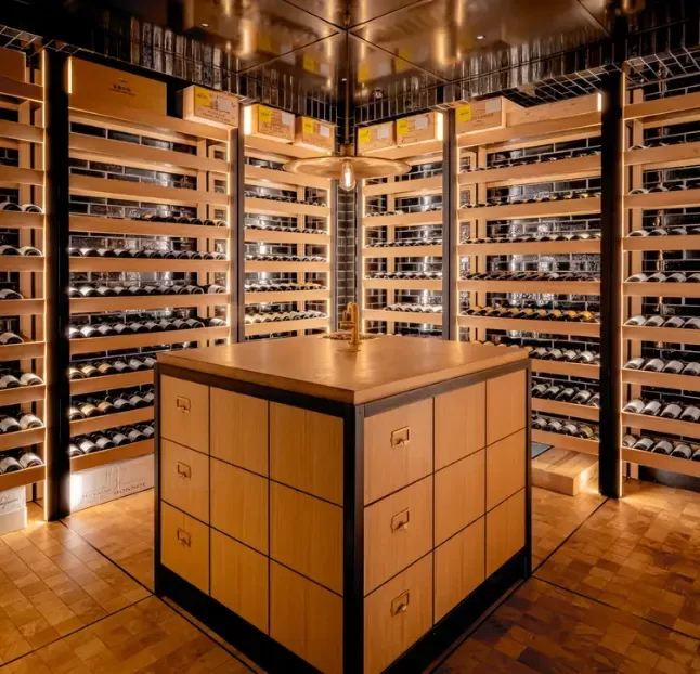 A wooden wine cellar lit up with a centre countertop.