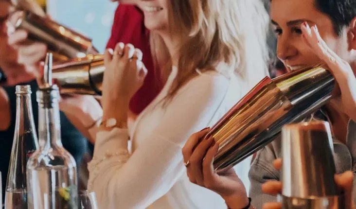 Women holding cocktail shakers in a bar setting.