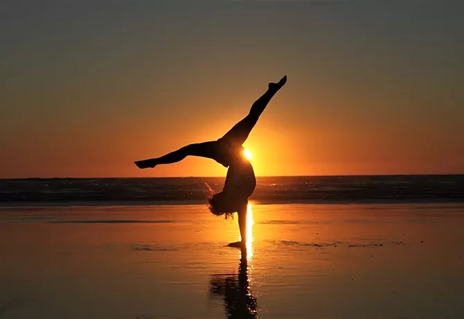 Women in handstand yoga pose in the sea shore with the sunset behind her