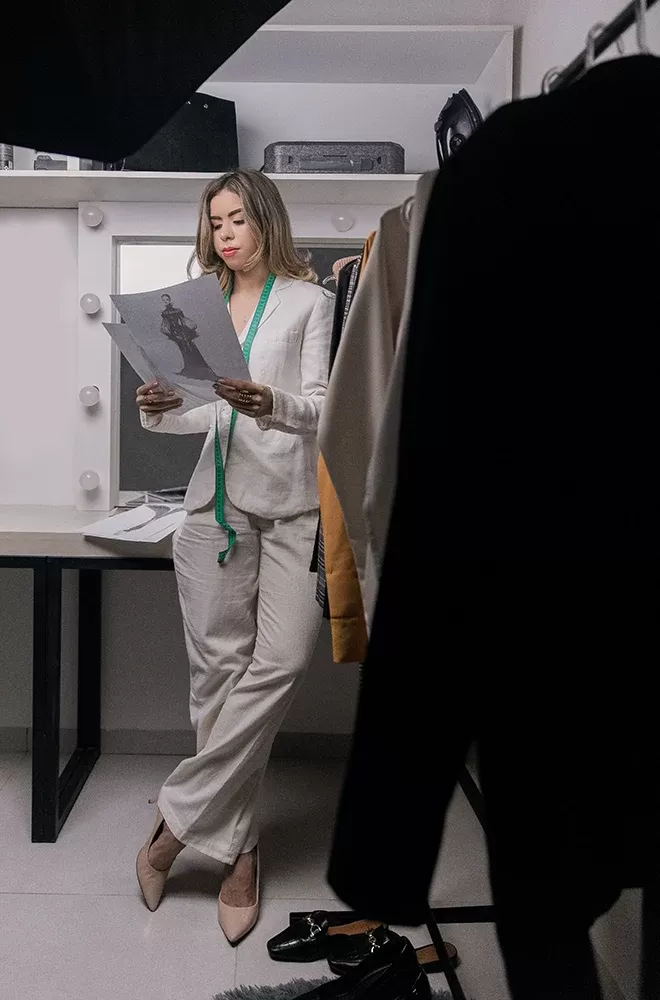 Designer with drawn designs stood in dressing room with a rack of clothing items
