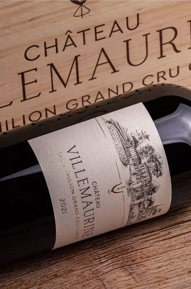 A bottle of Château Villemaurine wine rests on a wooden table, representing the essence of Saint-Émilion's winemaking tradition.
