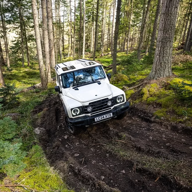 White INEOS Grenadier - ‘son of Defender’ car created by Sir Jim’s lieutenants off-road driving forest, mud and trees in the Cairngorms, Scotland.