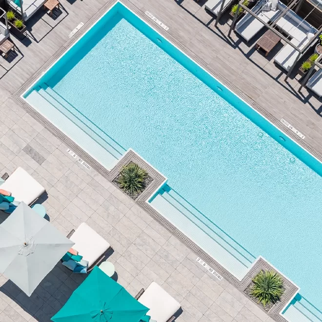 Birdseye view of baby blue pool with blue sun umbrellas surrounding it.