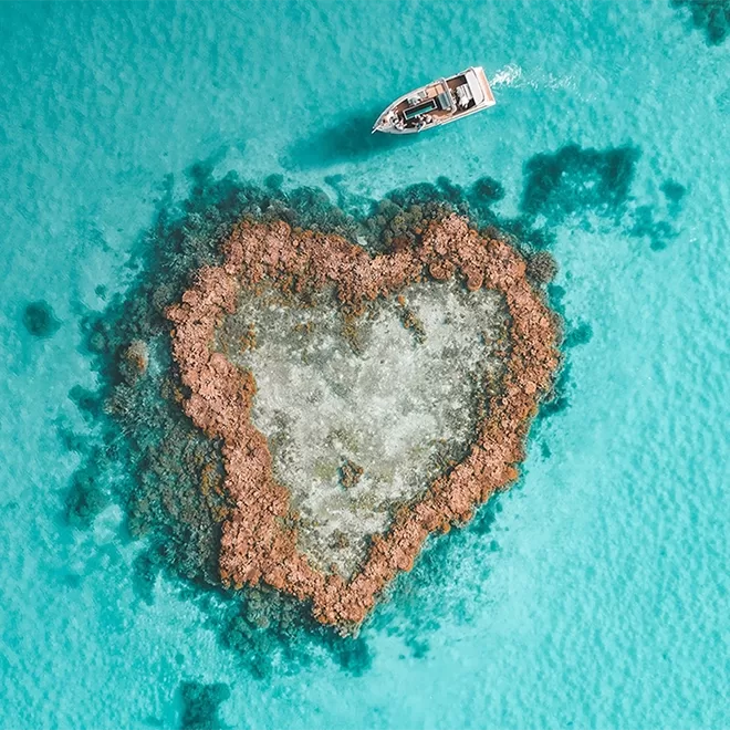 Arial view of yacht travelling in the clear blue sea around the heart-shaped island at qualia, Australia.