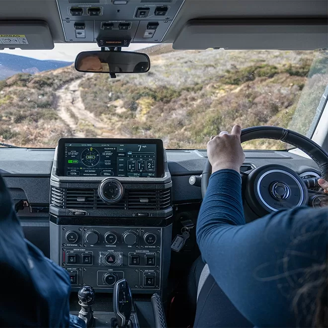 A person driving inside of INEOS Grenadier - ‘son of Defender’ car created by Sir Jim’s lieutenants with a view of the Cairngorms, Scotland.