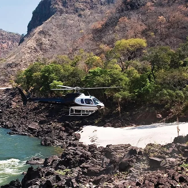 Helicopter flying and landing on sandy ground between rocky flour and canyons into Royal Chundu, Zambia.