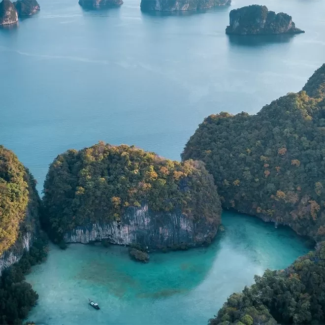 Arial view of boat travelling through sea filled with large rocks at Six Senses Yao Noi, Thailand.