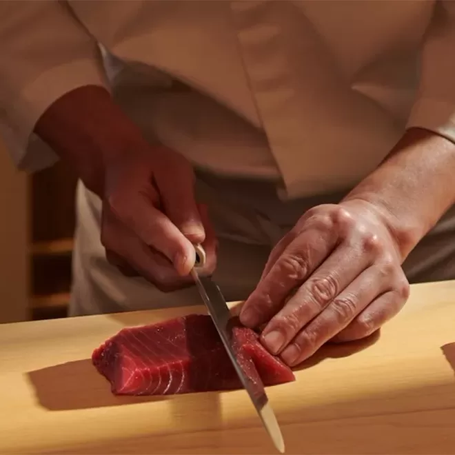 Chef in uniform carefully slicing a thick cut of tuna fih with a professional chef's knife at Sushi Kanesaka, London.