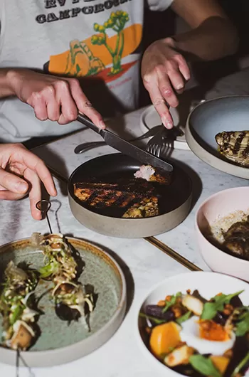 People sat eating plates of food on a table at Caia, London