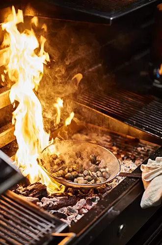 Food in a pan cooking on an open fire at Caia, London