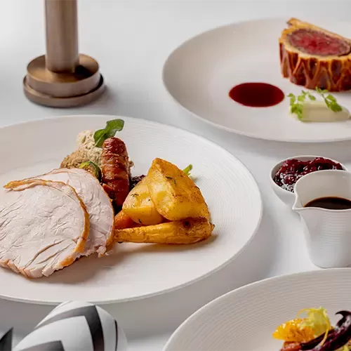Delicious and elegantly presented Christmas dinner dishes including the classic turkey, roast potatoes and stuffing as well as, beef wellington served on white plates with dipping sauces at Claridge’s Restaurant, Mayfair.