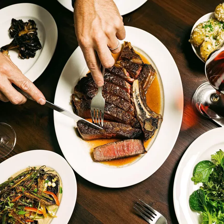 Selection of food with person cutting into steak at Gus's Chop House, Carroll Gardens, Brooklyn