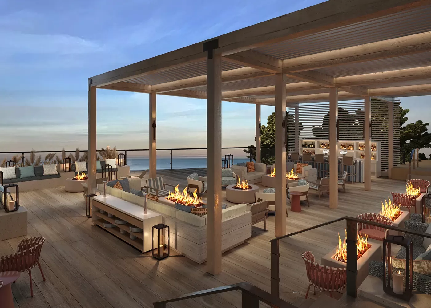 Rooftop lounge at sunset with modern seating, fire pits, wooden pergolas, and ocean views. Cozy sofas and chairs are arranged around low tables, creating an inviting atmosphere for relaxation.