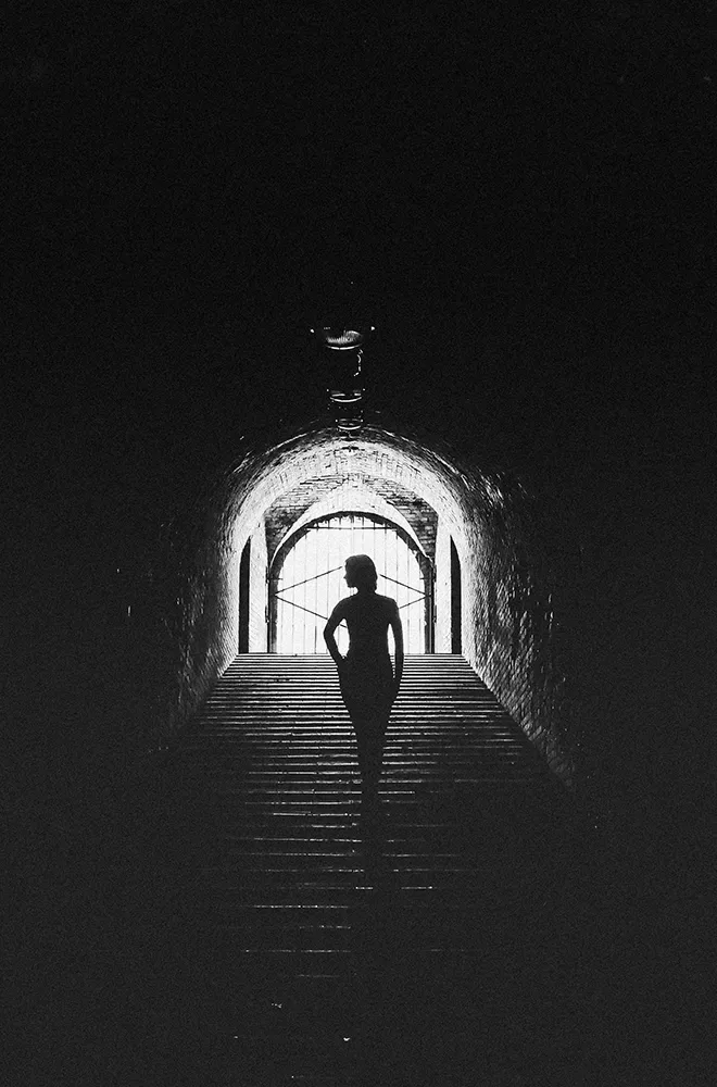 Black and white photo of a female silhouette walking up the stairs of an underground walkway