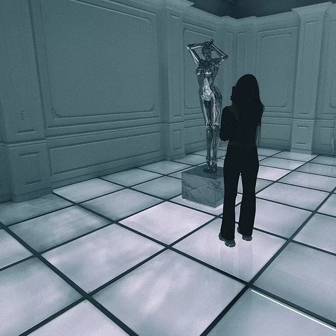 A contrast image of a woman in a gallery taking photo of a silver, robotic sculpture.