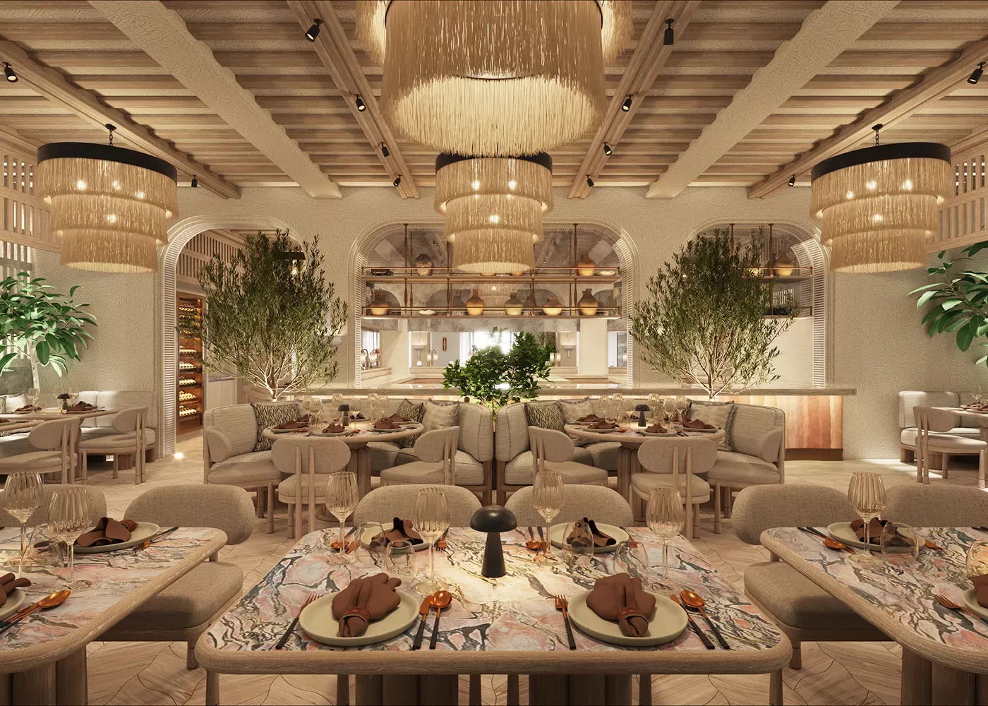 Elegant restaurant interior with soft lighting, large fringe chandeliers, cozy beige seating, marble-topped tables set with glassware and napkins, lush green plants, and an open kitchen in the background.