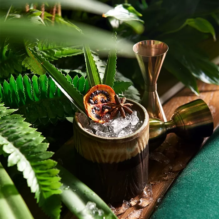 A vibrant cocktail served in a green bowl on a plank of wood, garnished with a fresh green leaf at Amazónico Monte-Carlo.