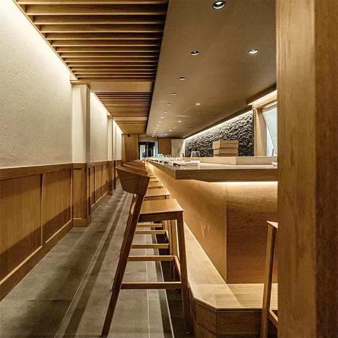 Inside Taku restaurant, a long bar with wooden stools and a sleek counter creates a welcoming atmosphere for guests.