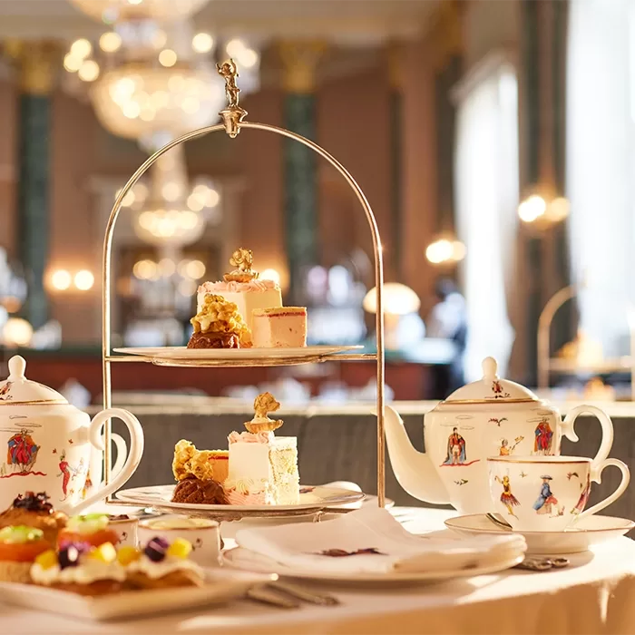 A table laid with a cake stand and delicious looking cakes surrounded by china tea pot and tea cups.
